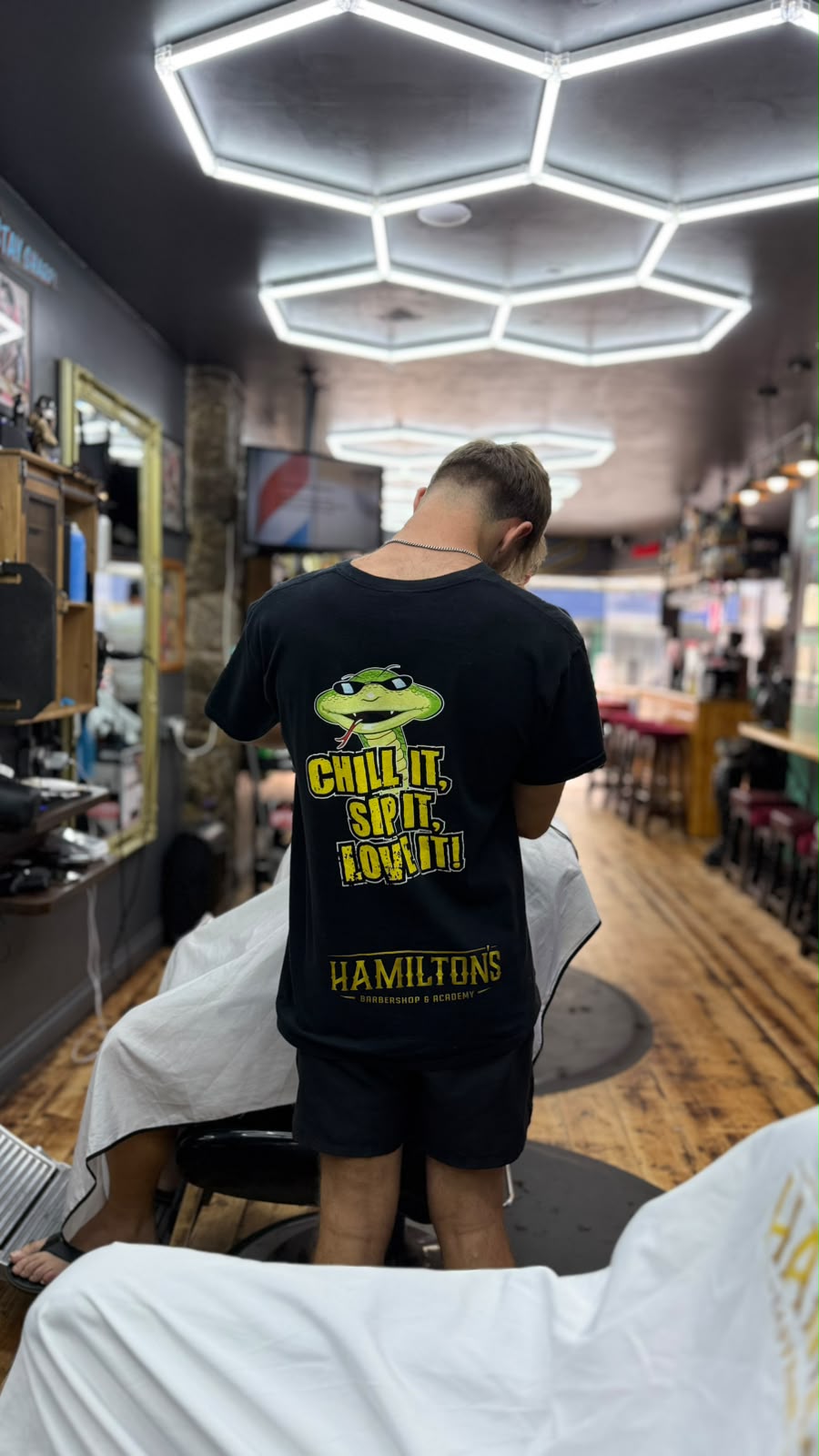 A Hamilton's barber in a branded t-shirt working on a client's haircut in the shop